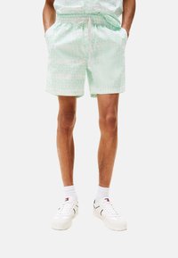 Pantaloni da bagno verde chiaro con motivo, dotati di vita elasticizzata e coulisse. Abbinati a scarpe da ginnastica bianche e calze bianche.
