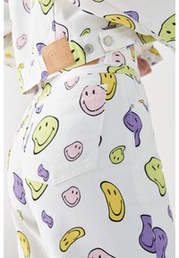 Tejido de mezclilla blanca con patrones de caras sonrientes coloridas en amarillo, rosa, verde y púrpura. Incluye una etiqueta de cuero de marca en la cintura.