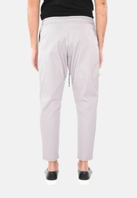 Pantaloni grigi chiari con vita elasticizzata, dotati di un cordoncino e tasche laterali. Il materiale è liscio con un design slim-fit.