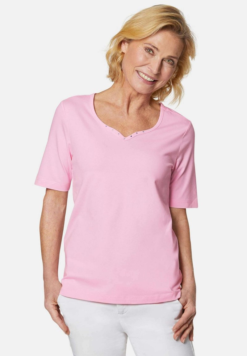 Rosa Kurzarm-T-Shirt mit V-Ausschnitt und dekorativen Nieten entlang des Ausschnitts. Aus weichem Stoff, entworfen für Komfort.