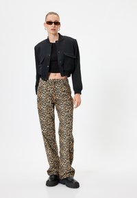 Black cropped bomber jacket, fitted black top, and loose leopard print pants. Black chunky shoes and rectangular sunglasses complete the look.