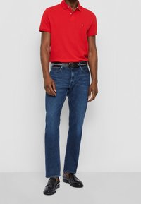 Polo rouge, jeans bleus, ceinture noire et mocassins noirs. Design simple, manches courtes, coupe droite et texture lisse.