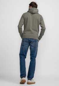 Sudadera con capucha gris de acabado texturizado, combinada con jeans de mezclilla azules. Zapatillas blancas con suela de goma marrón.