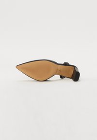 Black pointed-toe pump with a smooth upper, block heel, and textured rubber sole. Gold logo accents on the insole.