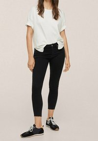 Top blanco de manga corta combinado con jeans negros ajustados y zapatillas deportivas negras con cordones blancos y acentos en marrón claro.