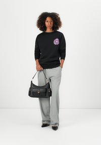 Black sweatshirt with a colorful floral print on the chest, paired with high-waisted gray pleated trousers and a black handbag with a buckle.
