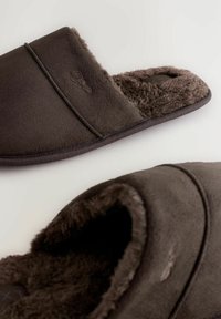 Brune ruskinds slippers med blød pelsforing, design med lukket ryg og subtilt brandingsdetalje nær top sømmen. Flad struktureret sål.