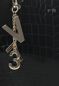 Borsa a tracolla in pelle nera con texture a coccodrillo, dotata di una catena dorata e audaci charm metallici: una lettera "V" e il numero "3".