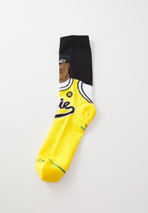 Calcetines amarillos con un tobillo negro y un gráfico de una persona vistiendo una camiseta amarilla. Tejido texturizado con un diseño colorido.