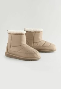 Stivaletti alla caviglia imbottiti beige con superficie texturizzata, fodera in pelliccia sintetica nella parte superiore e suola piatta in gomma. Presentano dettagli cuciti sui lati.