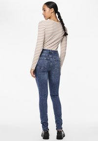 Høyt midje mørkeblå jeans med en tettsittende design, med baklommer og kombinert med en beige og hvit stripete langermet topp.