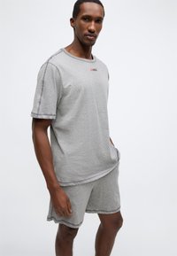 Σετ γκρι βαμβακερό μπλουζάκι με στρογγυλή λαιμόκοψη και κοντά μανίκια, και σορτς, με αντιθέτη ραφή. Λεπτομέρεια λογότυπου στο στήθος.