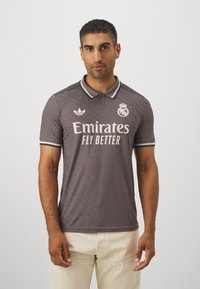 Grå polo skjorte med subtilt mønster, der har hvid "Emirates Fly Better" logo og emblem, mørkeblå krave og ærme detaljer, fremstillet af åndbart stof.