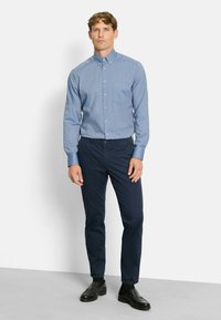 Lichtblauw overhemd met knopen en een borstzak, gedragen met donkerblauwe broek en zwarte schoenen, met een gepolijste afwerking en een slim-fit ontwerp.