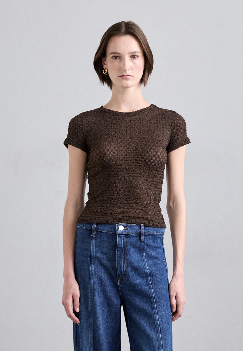 Hnědý texturovaný top s krátkým rukávem, fitted siluetu a kulatým výstřihem, spárovaný s modrými jeansy s vysokým pasem.