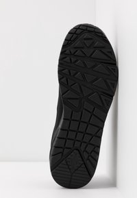 Semelle de sneaker noire avec un motif de relief géométrique. Matériau en caoutchouc durable, présentant des formes triangulaires et rectangulaires pour une meilleure adhérence.