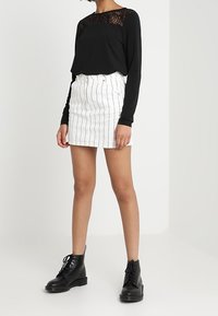 Svart långärmad topp med spetsdetaljer på axlarna, kombinerad med en vit randig minikjol och svarta snörade ankelstövlar.