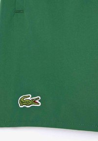Grünes Baumwollhemd mit gesticktem Krokodil-Logo in Weiß und Grün mit roten Akzenten, glatte Textur und leichtes Design.
