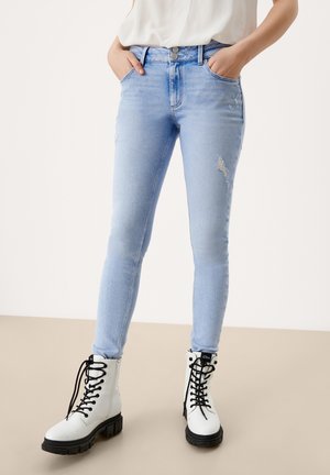 Jeans skinny de color azul claro con detalles desgastados, combinados con botas de combate blancas con cordones, que presentan suelas negras y goma gruesa y texturizada.
