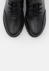 Botas de cuero negro con punta redonda, cordones frontales y cuellos acolchados. Las suelas son texturizadas para mayor tracción. Acabado suave y detalles de costura visibles.