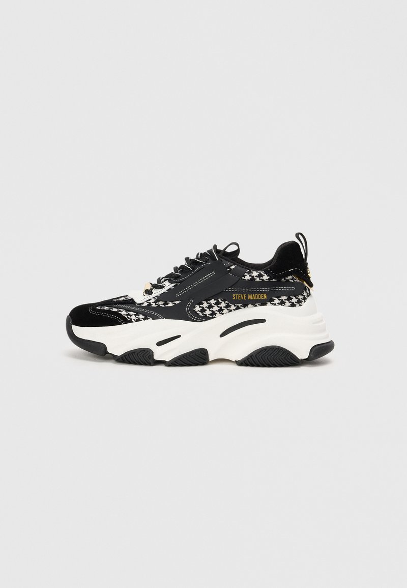 Melnbaltas sneakers ar masīvu dizainu, suņu zobu rakstu, gludām un tekstūru materiāliem, kā arī biezā baltā zole.