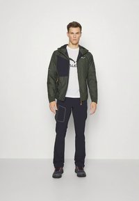 Roheline kerge jope tumesinise plaastri ja lukustusega ees, elastsete varrukaservadega, kantud valge T-särgi ja tumesiniste küljetaskutega pükstega.