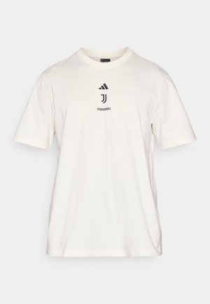 T-shirt en coton blanc avec un col rond, des manches courtes, et un graphisme central avec du texte noir et des accents, incluant le logo Adidas.