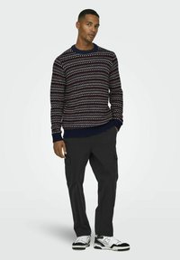 Pull en tricot à motif marin avec un col contrasté, porté avec un pantalon cargo noir et des baskets blanches avec des accents noirs.