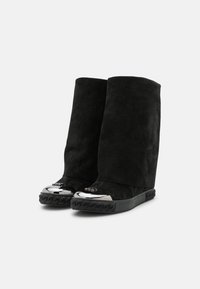 Botas de ante negro con una caña alta y estructurada, punteras negras brillantes y suelas negras texturizadas con un diseño trenzado.