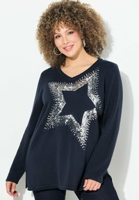 Marineblauer Sweater mit langen Ärmeln, V-Ausschnitt und einem großen silbernen Paillettensternmuster auf der Vorderseite. Strukturierter Stoff mit seitlichen Schlitzen.