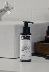 Flacon-pompe en plastique noir étiqueté « STMT » avec texte blanc, shampooing de 80 ml, posé sur une surface gris clair à côté d'un contenant en bois.