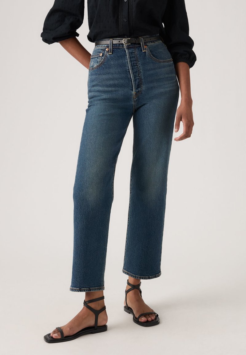 Μπλε τζιν με ψηλή μέση και ίσια γραμμή, με ξεθωριασμένη όψη, κλασικό σχέδιο με πέντε τσέπες και ραμμένα διακοσμητικά, σε συνδυασμό με μαύρα σανδάλια.