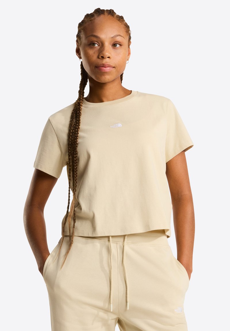 Lichtbeige cropped t-shirt gemaakt van zacht katoen, met een klein wit logo op de borst. Korte mouwen en een ontspannen pasvorm.