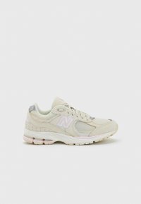 Light beige athletic shoe with mesh details, a pink logo, and gray accents. Features a cushioned sole with visible air pockets for comfort.
