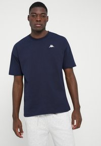 Marineblaues Baumwoll-T-Shirt mit kurzen Ärmeln, geripptem Ausschnitt und einem kleinen weißen Logo auf der oberen linken Brust. Glatte Textur, lässige Passform.