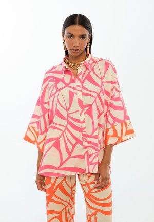 Camisa de manga corta con botones en color crema con patrones llamativos de hojas en rosa y naranja. Combinada con pantalones a juego con el mismo estampado y colores.