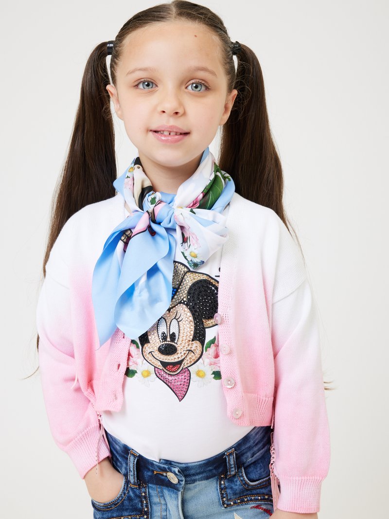 T-shirt bianco con un design scintillante di Minnie Mouse, cardigan ombré rosa, e una sciarpa floreale azzurro chiaro, abbinati a pantaloni corti in denim.