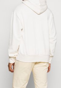 Witte hoodie met een ontspannen pasvorm, geribbelde mouw- en zoomranden. Zachte stof met een gladde textuur en zonder zichtbare patronen of hardwaredetails.