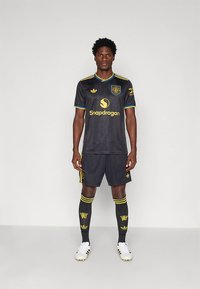 Juoda futbolo apranga su geltonais akcentais, ant kurios yra logotipas ir užrašas „Snapdragon“. Komplekte yra derančios šortai, kojinės ir balti futbolo bateliai.