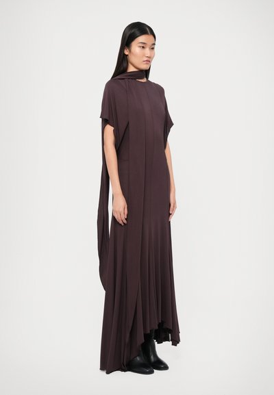 Dark brown, flowy, long dress with short sleeves, asymmetrical hem, and draped detail, paired with black ankle boots. Smooth fabric texture.