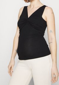 Svart ärmlös topp med V-halsringning, med en knutdetalj fram. Tillverkad av mjukt, stretchigt tyg som kompletterar strukturerade beige byxor.