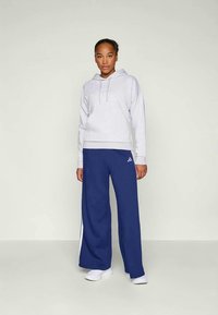 Sweatshirt capuz cinza claro com cordões, combinado com calças largas azul marinho com riscas brancas laterais. Ambos feitos de um tecido macio.