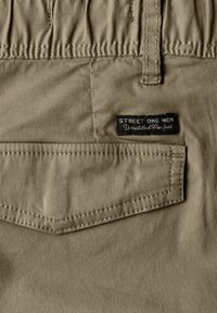 Poche arrière d'un pantalon beige pour homme avec une ceinture élastique et une étiquette noire "Street One Men Unmatched Comfort".