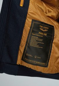 Bunda PME Legend s hustým námořnickým vlněným vnějším materiálem, zlatou prošívanou podšívkou a černou pečetí s produktovými specifikacemi.