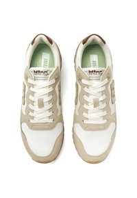 Zapatillas beige y blancas con textil de malla y detalles de cuero suave, que presentan un diseño de cordones y suelas de goma marrón. Plantillas verdes.