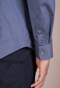 Lichtblauw overhemd met knopen, voorzien van een gladde textuur, lange mouwen en contrasterende manchetknoopjes. Gecombineerd met donkere, gestructureerde broek.