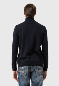 Dunkelblauer Rollkragenpullover mit geripptem Kragen und Ärmeln, kombiniert mit hellblauen Jeans aus Denim mit dekorativer Stickerei auf den Gesäßtaschen.