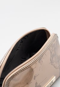 Bustina beige con cerniera, caratterizzata da un design con mappa del mondo, superficie testurizzata e fodera interna nera. Dettagli hardware color oro.