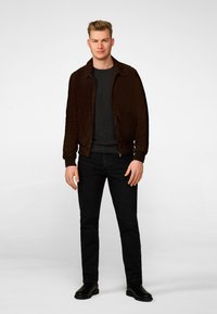 Brown suede bomber jacket with a zippered front, worn over a dark gray sweater, paired with black jeans and black ankle boots.
