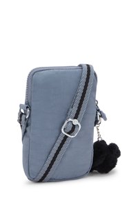 Liten blå crossbody-väska med svart och grå randig justerbar rem och en svart fluffig pom-pom nyckelring hängande från dragkedjan.